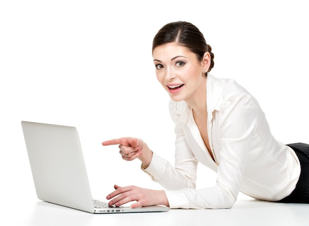 Vrouw met laptop wijst naar het scherm in wit overhemd liggend op de vloer - geïsoleerd op wit.