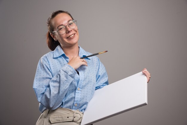 Vrouw met leeg canvas en penseel op grijze achtergrond