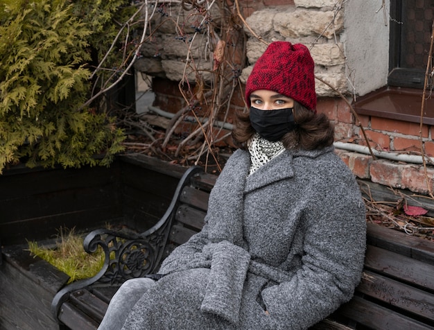 Vrouw met medisch masker buiten op de bank