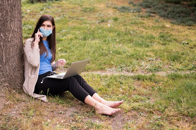 Vrouw met medisch masker die aan laptop in openlucht werken