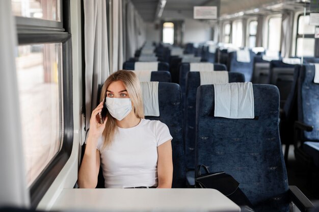 Vrouw met medisch masker die met de openbare trein reist en smartphone gebruikt