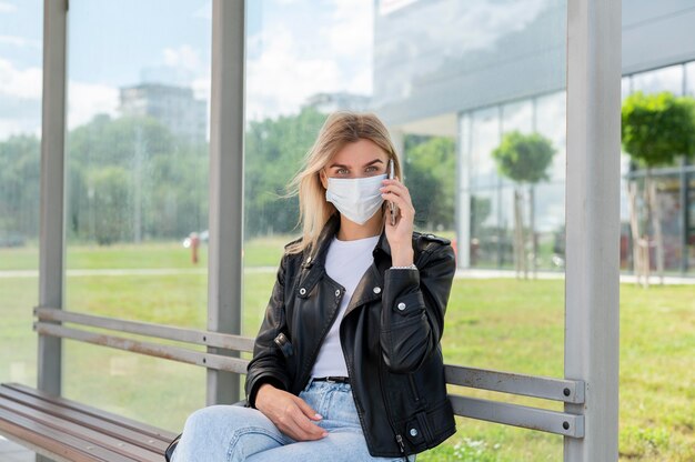 Vrouw met medisch masker die smartphone gebruikt tijdens het wachten op de openbare bus