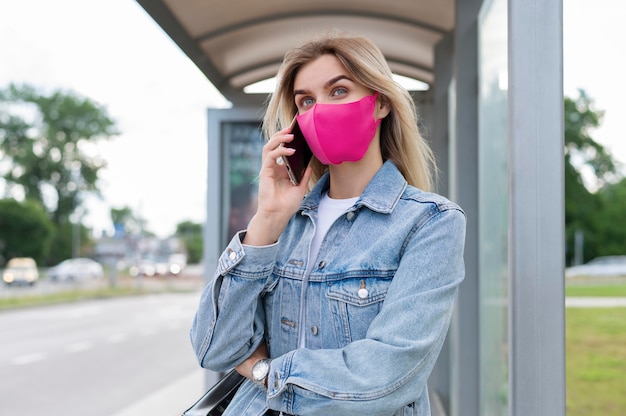 Vrouw met medisch masker die smartphone gebruikt tijdens het wachten op de openbare bus