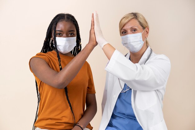 Vrouw met medisch masker geeft haar dokter een high-five na het krijgen van een vaccin