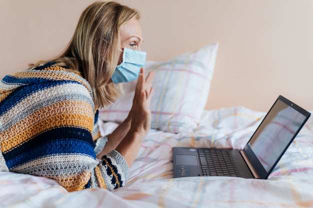 Vrouw met medisch masker in quarantaine thuis met laptop