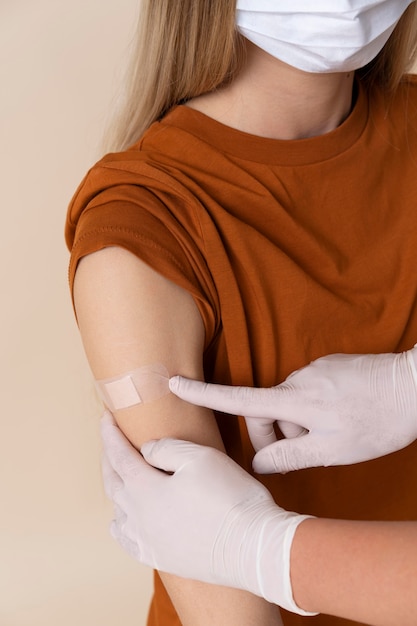 Vrouw met medisch masker krijgt sticker op arm na vaccinatie