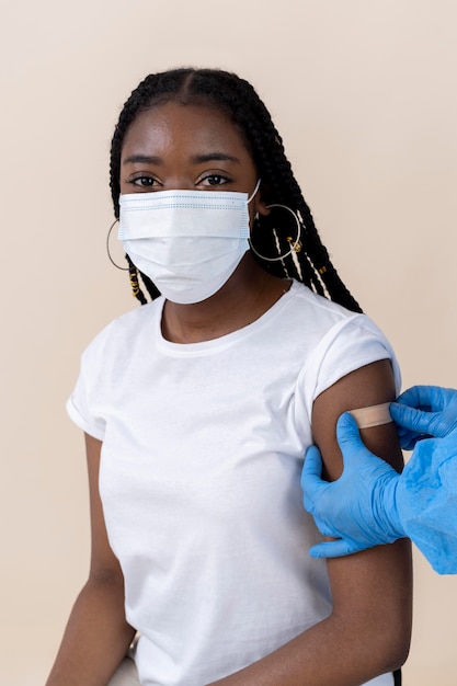 Vrouw met medisch masker krijgt sticker op arm na vaccinatie