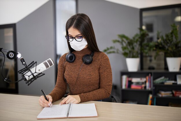 Vrouw met medisch masker op de radio met microfoon en notitieboekje