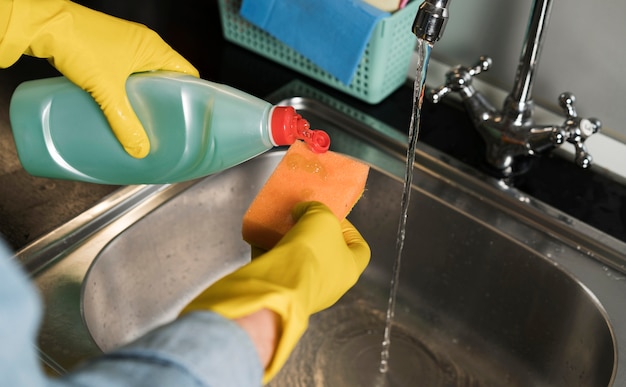 Vrouw met rubberhandschoenen die de gootsteen schoonmaken