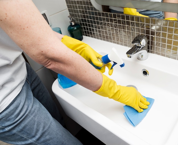 Vrouw met rubberhandschoenen die de gootsteen schoonmaken