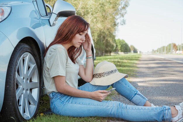 Vrouw met smartphone die tegen haar auto leunt