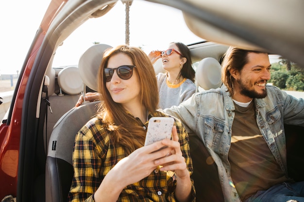 Vrouw met smartphone en positieve man in auto dichtbij dame die uit auto leunt