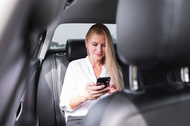 Vrouw met telefoon in auto achterbank