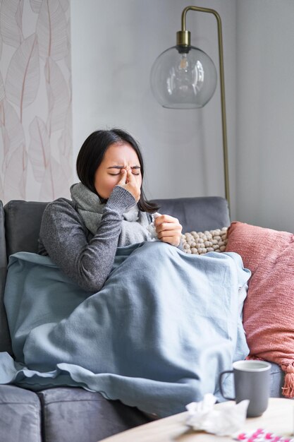 Vrouw met temperatuur hoesten met symptomen van griep, griep of verkoudheid zittend in warme kleren aan