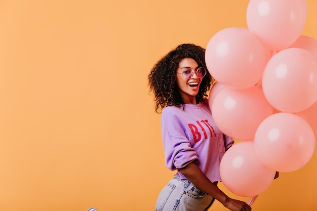 vrouw met trendy kapsel poseren op oranje afterparty. lachen mooie zwarte meisje met ballonnen.