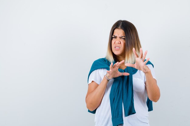 Vrouw met vastgebonden trui die stopgebaar in wit t-shirt toont en er walgelijk uitziet. vooraanzicht.