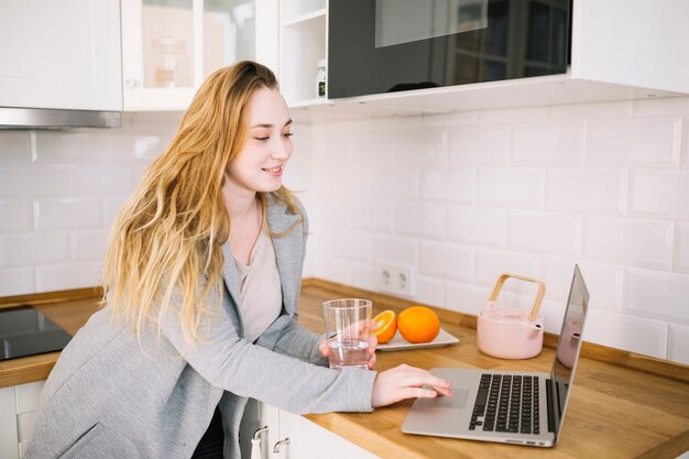 Vrouw met water die laptop in keuken met behulp van