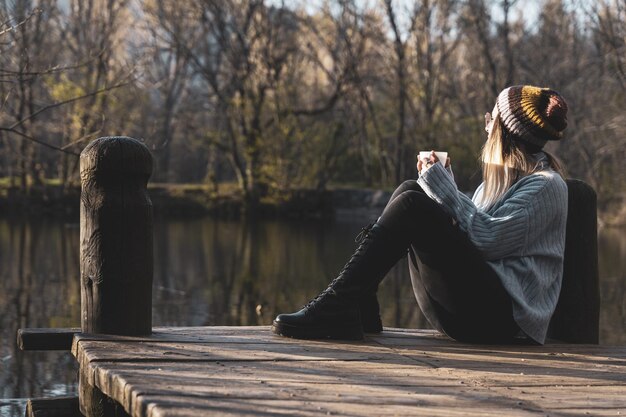 Vrouw ontspannen in de houten pier van het meer met een kopje koffie