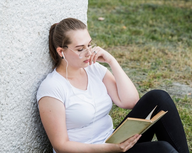 Gratis foto vrouw ontspannen met boek bij parkmuur