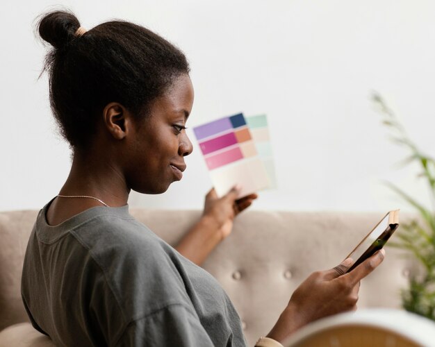 Vrouw op de bank die een plan maakt om huis opnieuw in te richten met behulp van tablet en kleurenpalet