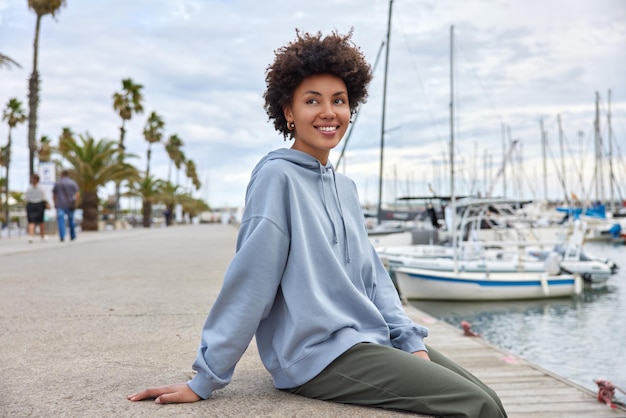 vrouw poseert alleen op de pier kijkt vrolijk weg geniet van uitzicht op de zee en goed weer draagt een sweatshirtbroek die in de verte is gericht. Vrouw brengt vrije tijd door in zeehaven