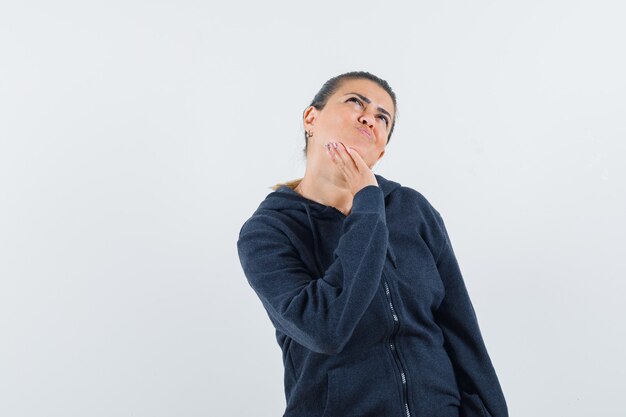 Vrouw raakt haar kaak in hoodie aan en kijkt peinzend. vooraanzicht.