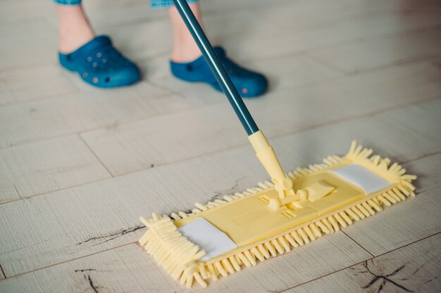 Vrouw schoonmaak vloer met gele dweil thuis. microfiber dweil geïsoleerd op een witte houten vloer achtergrond, close-up, binnenshuis