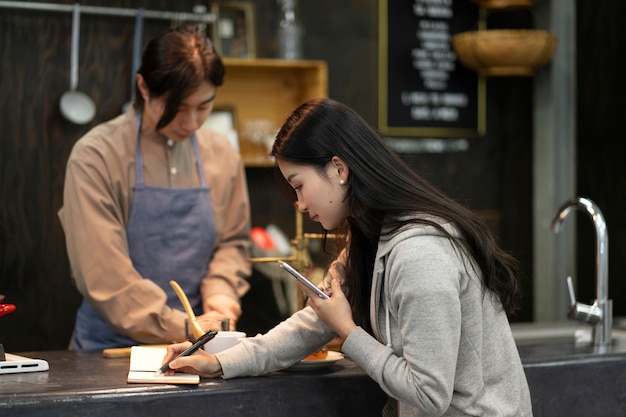 Vrouw schrijft op een notitieboekje terwijl de man kookt in een restaurant