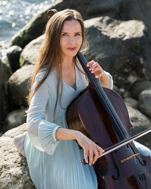 Vrouw speelt cello aan zee met rotsen