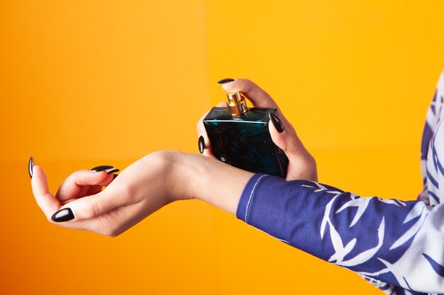 Vrouw sprenkelt parfum op haar hand op een oranje achtergrond Premium Foto