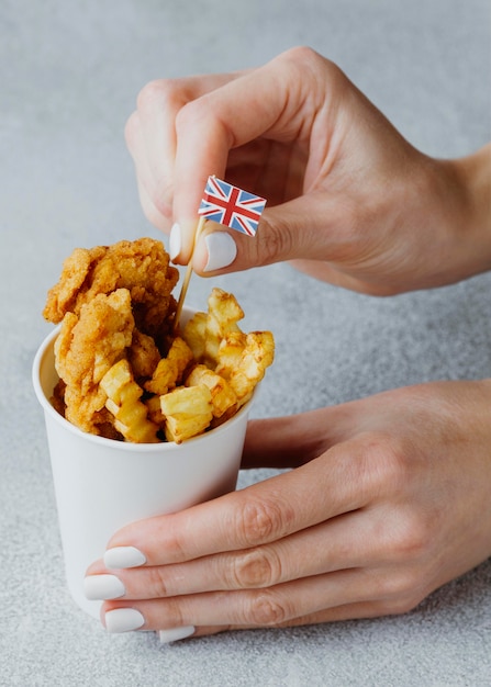 Vrouw steekt vlag van Groot-Brittannië in fish and chips schotel in kartonnen beker