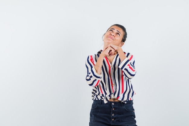 vrouw steunt kin op gevouwen handen in shirt, rok en kijkt hoopvol.