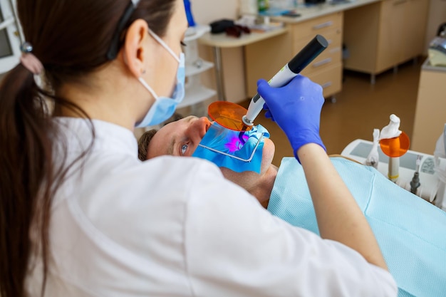 Vrouw tandarts onderzoekt de patiënt met instrumenten in de tandheelkundige kliniek. de arts maakt tandheelkundige behandeling op de tanden van een persoon in de stoel van de tandarts. selectieve focus