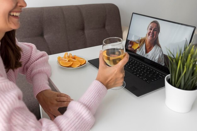 Vrouw thuis in quarantaine met een drankje met vriend via laptop