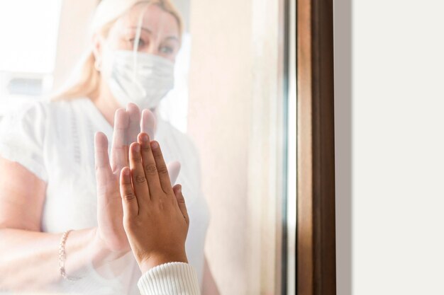 Vrouw thuis in quarantaine met medisch masker achter raam