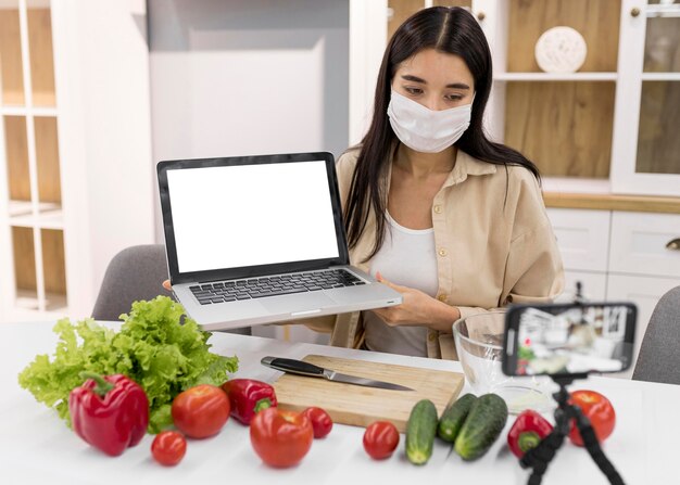 Vrouw thuis vloggen met groenten en laptop