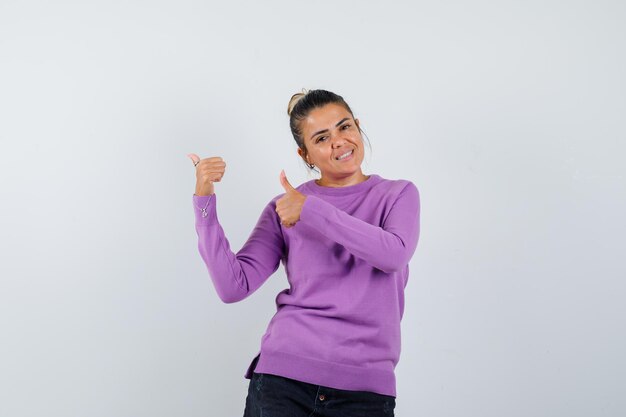 Vrouw toont dubbele duimen in wollen blouse en ziet er zelfverzekerd uit
