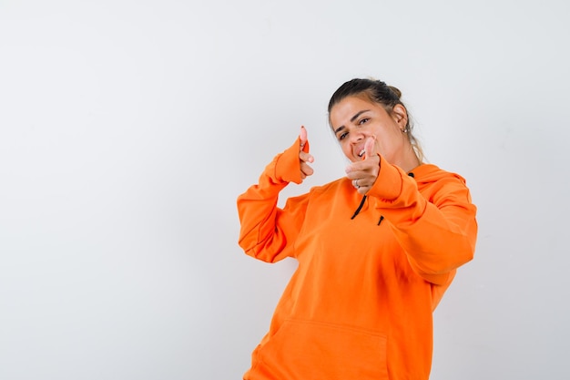 Vrouw toont geweergebaar in oranje hoodie en ziet er gelukkig uit