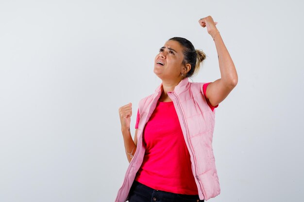 Vrouw toont winnaar gebaar in t-shirt, vest en ziet er gelukkig uit