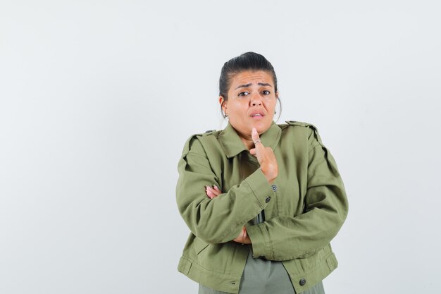 Vrouw toont zichzelf in vragend gebaar in jasje, t-shirt en kijkt verbaasd.