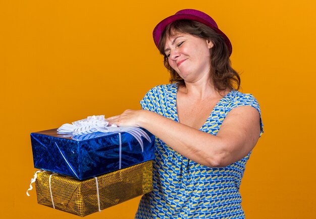 Vrouw van middelbare leeftijd in feestmuts met verjaardagscadeautjes die er verward uitziet
