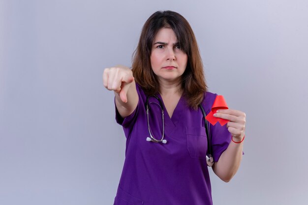 Vrouw van middelbare leeftijd verpleegster uniform dragen en met stethoscoop houden rood lint een symbool van de strijd tegen aids wijzen ontevreden naar de camera boos en woedend met je staande over w