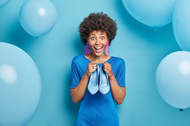 Gratis foto vrouw verkleedt zich voor speciale gelegenheid kiest schoenen met hoge hakken om te dragen bereidt zich voor op feest geïsoleerd op blauw