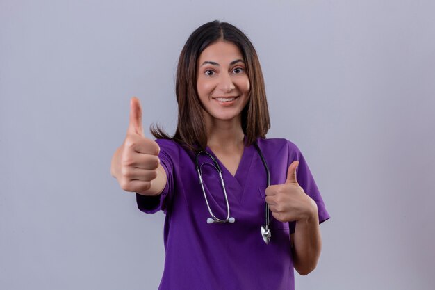 vrouw verpleegster in medisch uniform en met een stethoscoop met een zelfverzekerde glimlach op het gezicht zien thumbs up tonen succes staande op geïsoleerde wit