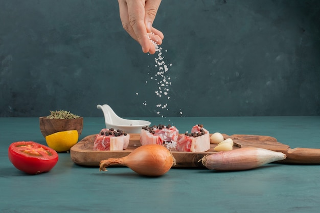 Gratis foto vrouw voegt zout toe aan stukken ongekookt vlees op blauwe tafel.