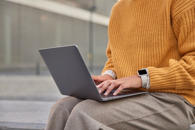 vrouw werkt aan nieuw project toetsenborden informatie op laptop draagt gebreide gele trui en broek