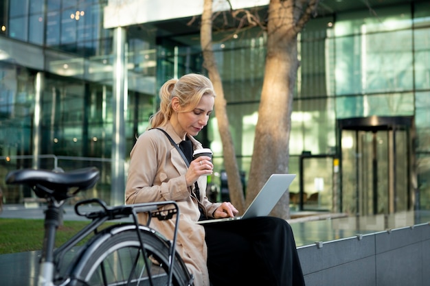 Vrouw werkt buiten aan haar laptop en drinkt koffie.