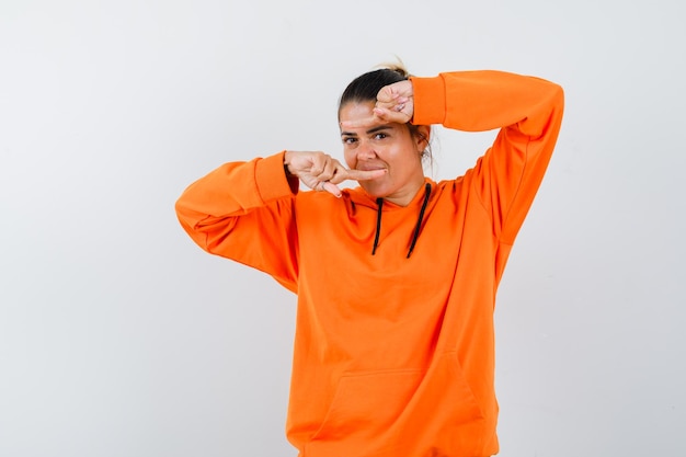Gratis foto vrouw wijst naar beide kanten in oranje hoodie en ziet er zelfverzekerd uit