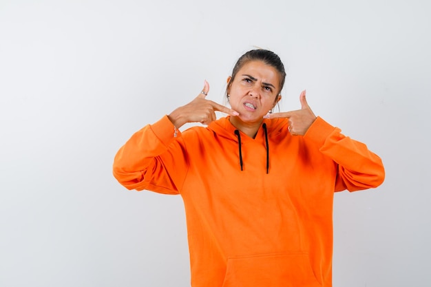Vrouw wijst naar zichzelf in oranje hoodie en ziet er zelfverzekerd uit
