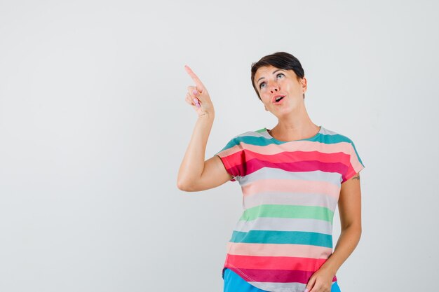 Vrouw wijzend op de linkerbovenhoek in een gestreept t-shirt en kijkt verbaasd, vooraanzicht.